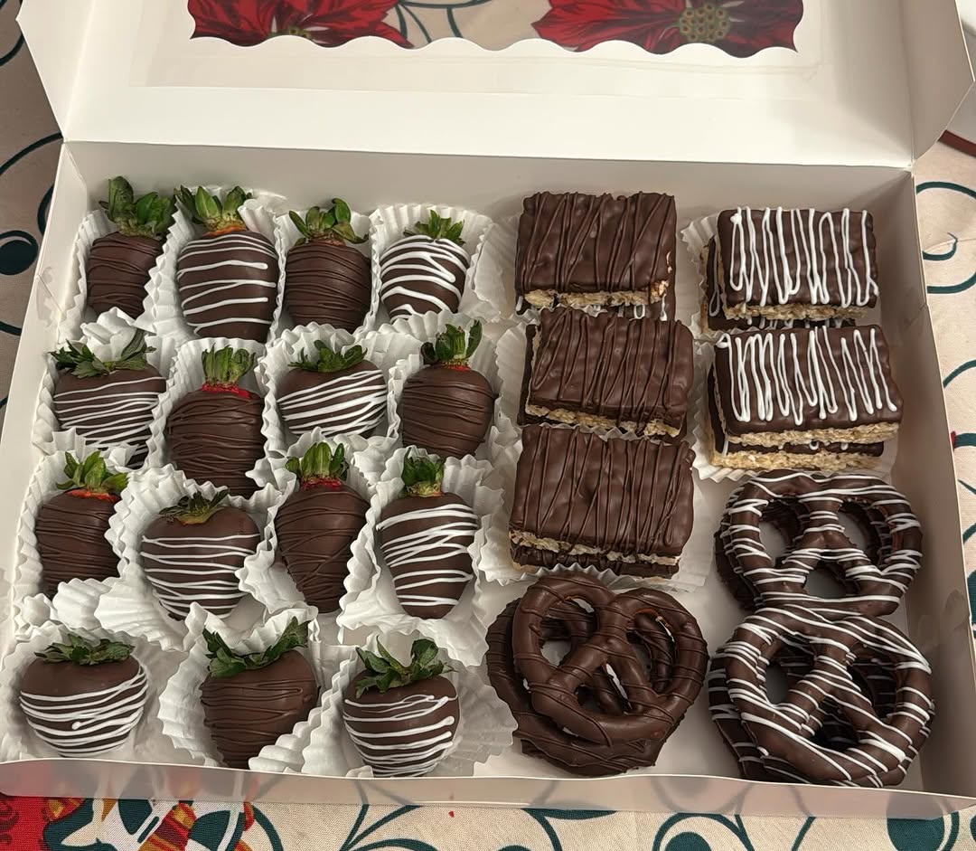 Large holiday box of dark chocolate strawberries, Rice Krispie bars, and pretzels, all decorated with white chocolate drizzle patterns.