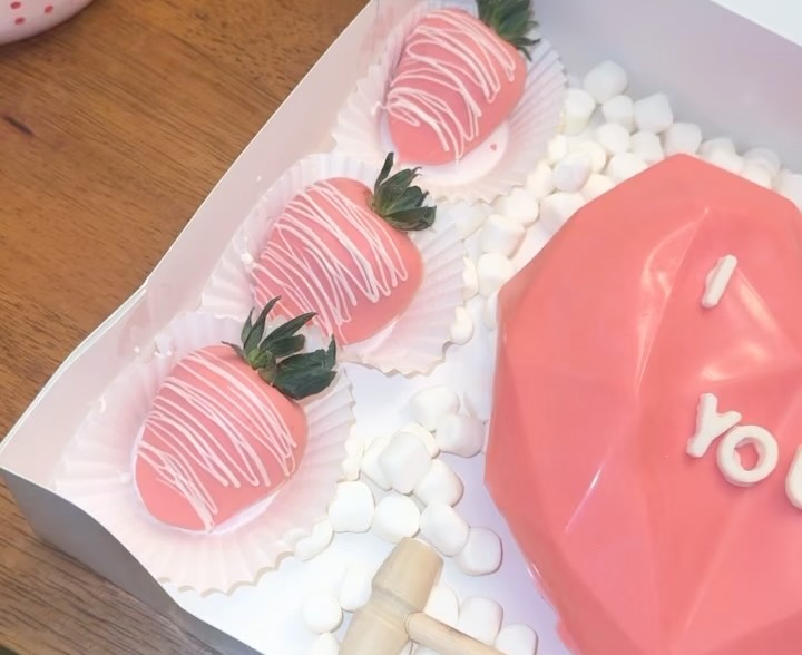 Close-up of three pink drizzled strawberries and partial view of a geometric faceted breakable heart with I LOVE YOU text.