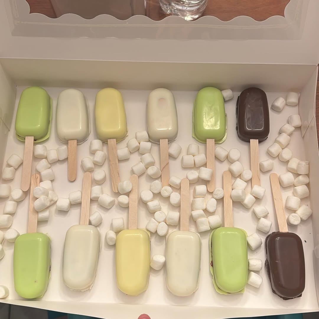 A dozen cakesicles in a beautiful green gradient from lime to sage to mint, creating a striking ombre effect with scattered marshmallows.