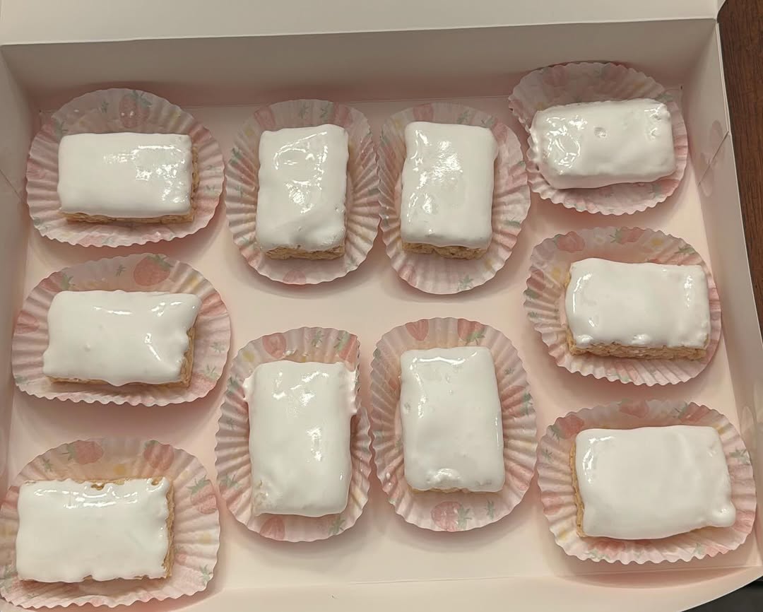 Ten white chocolate-dipped Rice Krispie treat bars arranged in a grid with charming strawberry-print paper liners.