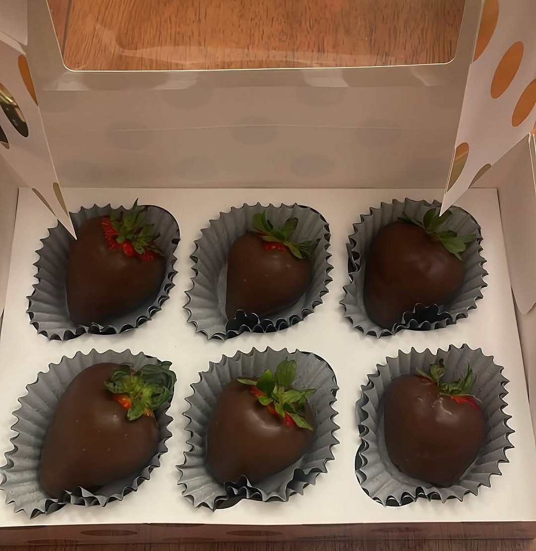 Half-dozen dark chocolate-covered strawberries in a decorative white box with gold polka dots, each berry in a blue-gray paper liner.