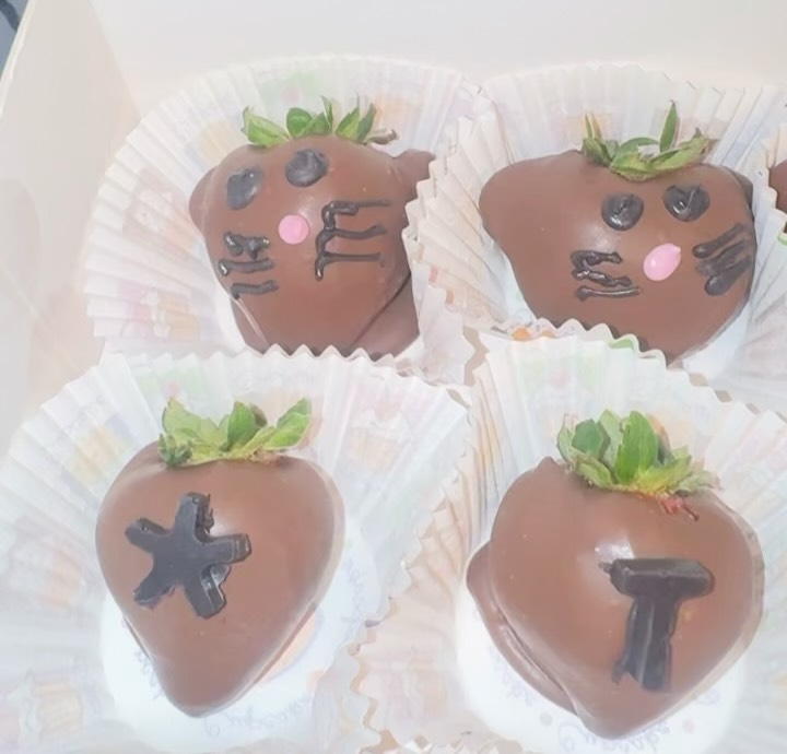 Close-up of four adorable cat-face chocolate strawberries with piped dark chocolate whiskers, dot eyes, and pink candy noses.