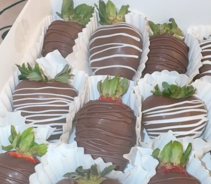 Close-up of dark chocolate strawberries with horizontal white chocolate drizzle stripes, showing fresh green stems contrasting with the glossy coating.