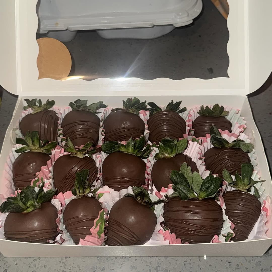 A dozen dark chocolate strawberries with additional dark chocolate drizzle lines in pink and white patterned liners, a classic elegant presentation.