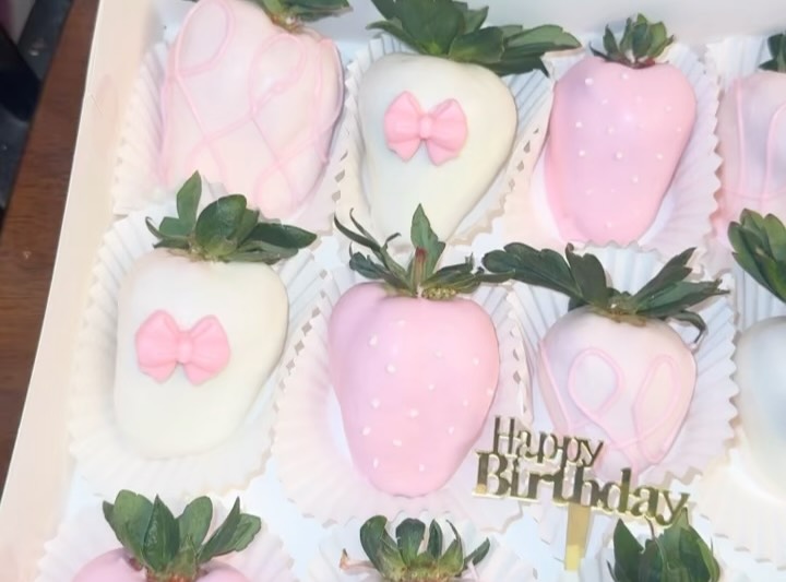 Close-up of artisan birthday strawberries showing detailed fondant bows, evenly spaced polka dots, and precise pink drizzle patterns.